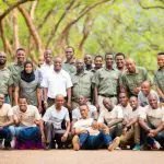 A group of people wearing matching shirts pose together outdoors, surrounded by trees, as if ready for a vibrant safari adventure.