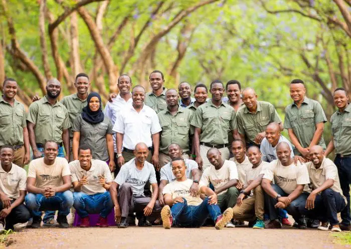 A group of people wearing matching shirts pose together outdoors, surrounded by trees, as if ready for a vibrant safari adventure.