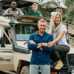 Four people are posed around a pristine safari vehicle; two are standing, and two are sitting. The setting suggests an exciting family adventure in Tanzania, possibly during a 10-day tour through the breathtaking safari parks.