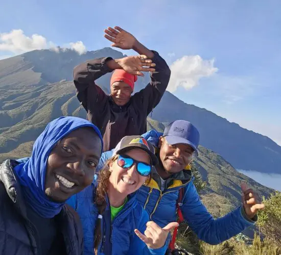 Four people smiling and posing for a selfie atop Mt Meru, capturing the breathtaking landscape during their trekking tour.