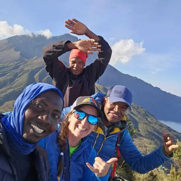 Four people smiling and posing for a selfie atop Mt Meru, capturing the breathtaking landscape during their trekking tour.