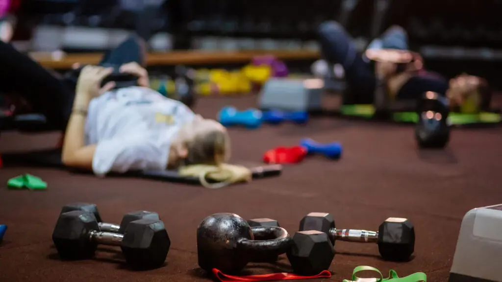 First-timers lying on exercise mats in a gym, with dumbbells, a kettlebell, and resistance bands scattered on the floor—perfect for starting your fitness plan or Kilimanjaro training.