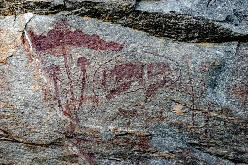 Ancient rock art in Tanzania depicts figures and shapes, possibly animals and plants, painted in reddish pigment on a rough stone surface—a must-see for those who travel or visit the region.