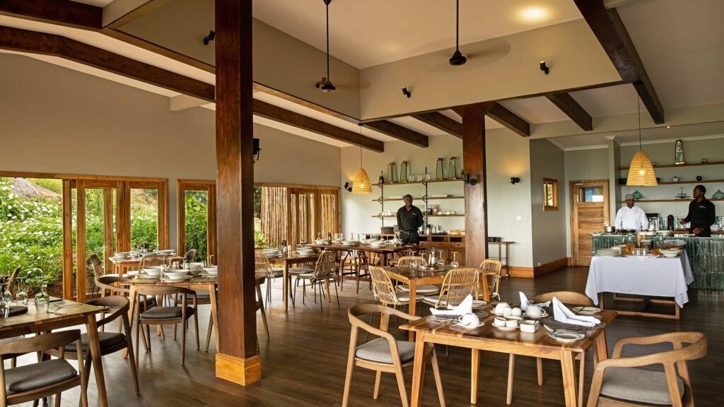 A modern restaurant dining area with wooden tables and chairs, set for service, with chefs preparing food at a counter in the background.