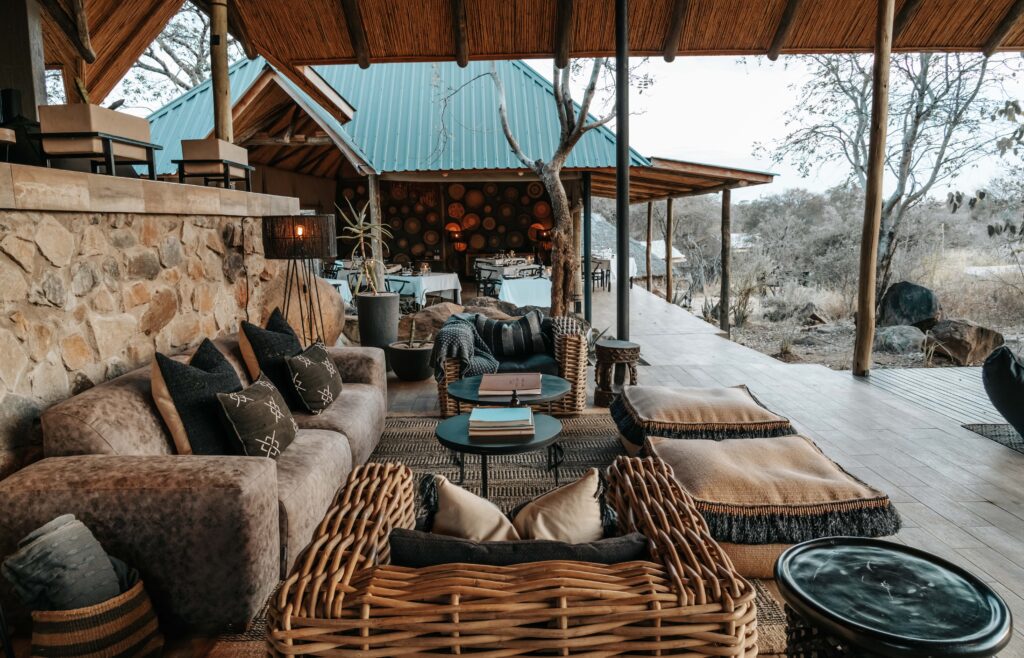 Open-air lounge area with wicker and upholstered furniture, cushions, and wooden tables, set under a thatched roof at Nimali Tarangire luxury safari lodge, offering views of Tarangire National Park’s dry, natural landscape.