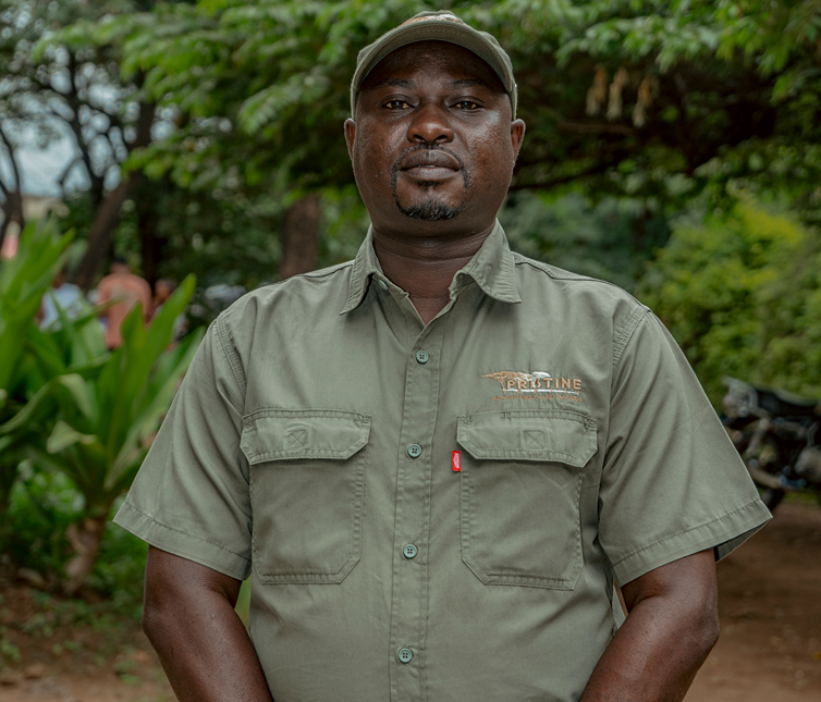 Meet the Team: A man wearing a green uniform shirt and cap stands outdoors in front of trees and foliage.