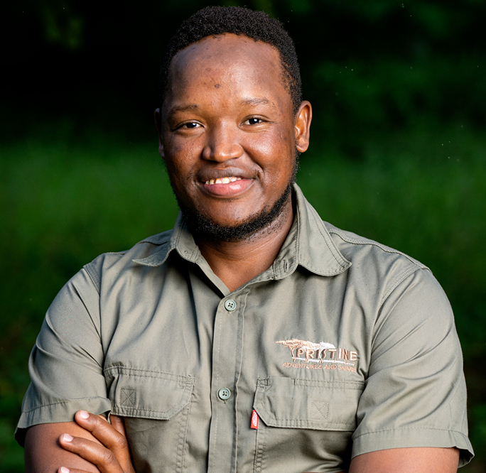 Meet The Team: A man in a green button-up shirt with the "PRISTINE" logo stands outdoors with arms folded, smiling at the camera. Green foliage is visible in the background.