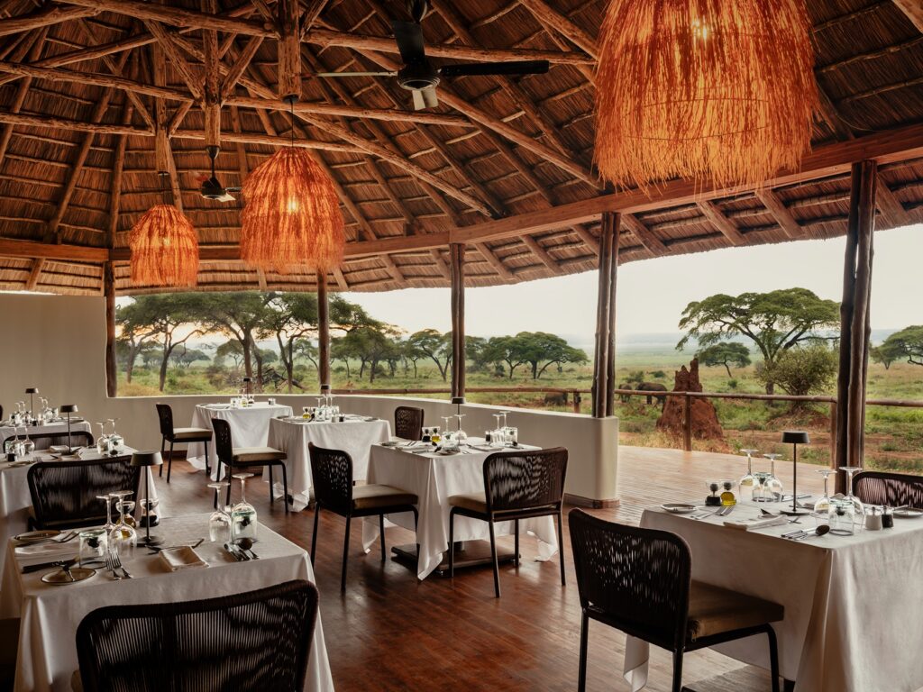 Open-air dining room at Sanctuary Swala with tables set for service, overlooking a Tanzania safari landscape featuring trees and a termite mound.